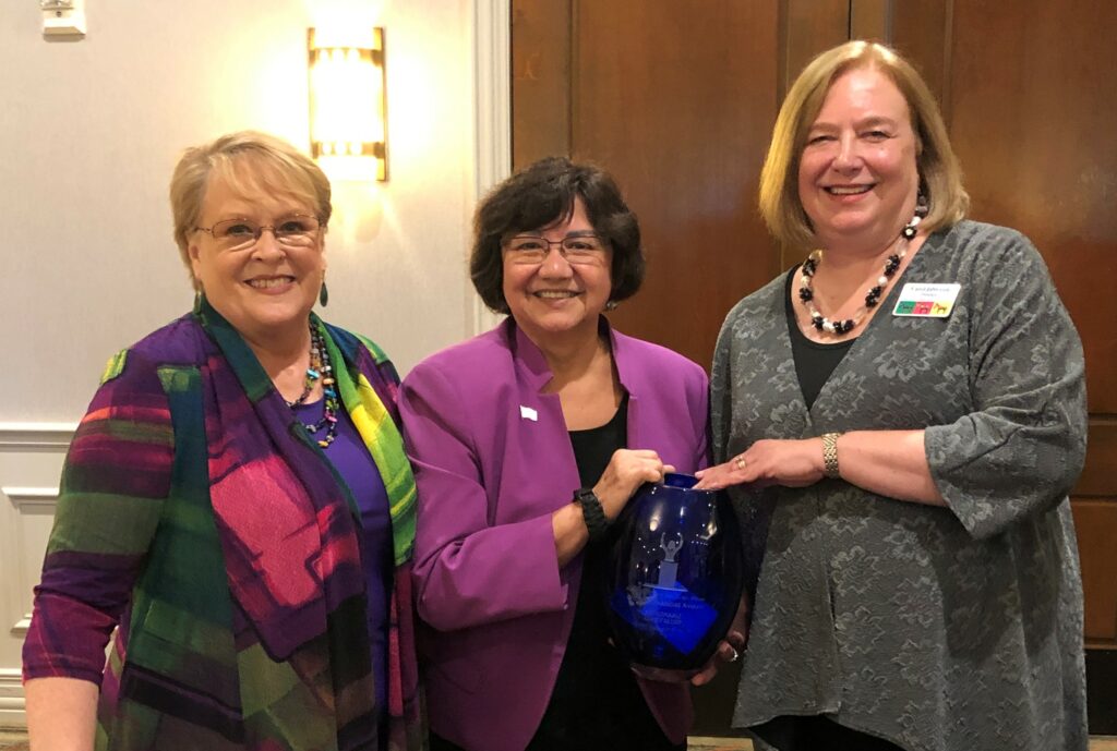 Three women standing next to each other holding a blue glass.